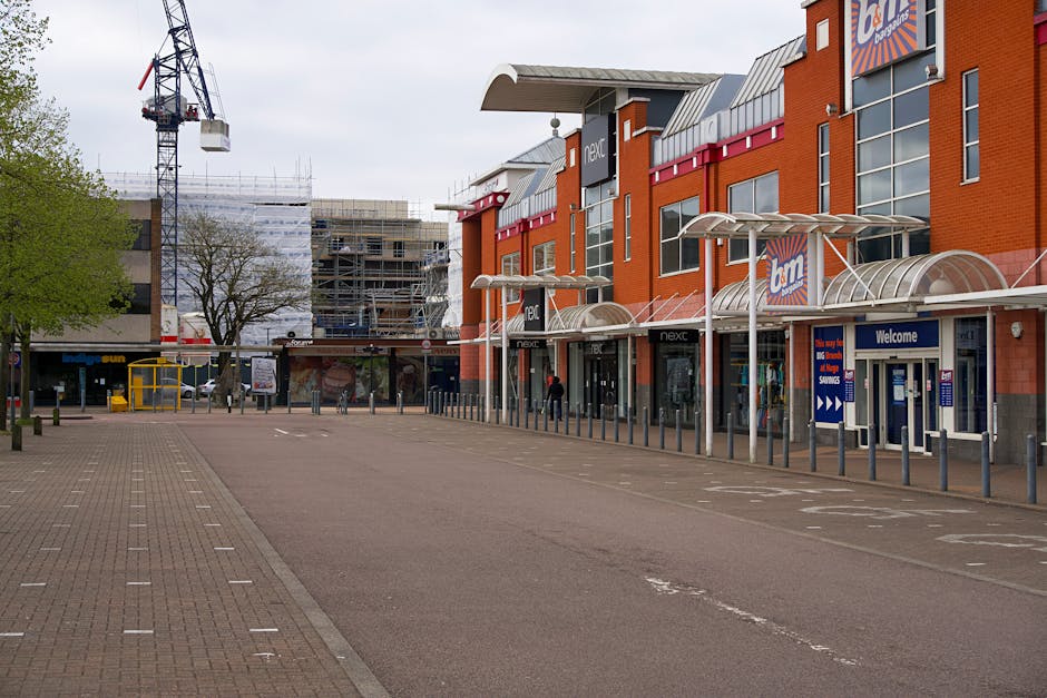 A vertical white signboard displaying the blue and white text 'Ealing Broadway' within a red circular symbol, positioned on a paved train platform. Behind the sign, a train with a silver body and red 